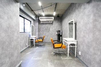 モダンなデザインの美容室内装、グレーの壁と床を特徴としたスタイリッシュなヘアサロンの鏡と椅子