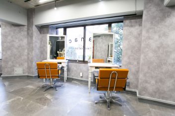 モダンなデザインの美容室内装、グレーの壁紙とオレンジのアクセントチェアが特徴のカットステーション