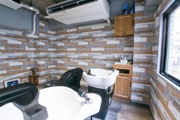 モダンでスタイリッシュな美容室の洗髪スペース、木目調の壁と白い洗髪ユニットが特徴的
