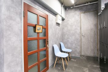 現代的なデザインの美容室の待合室、木製のドアとガラス窓、灰色の壁と床、モダンな青い椅子とロッカーが特徴