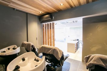モダンな美容室のシャンプーエリア、木材のアクセントとシックなインテリアデザインが特徴