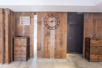 モダンで洗練された美容室の待合室、木製パネルの壁と装飾大時計、収納キャビネットが特徴的