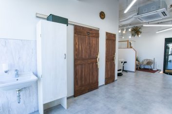 明るく清潔感のある美容室のインテリアで、木目調の扉、ホワイトの洗面台、快適な待合スペースが特徴的