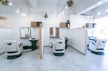 モダンで洗練されたデザインの美容室の内装、ホワイトのスタイリッシュなヘアサロンチェアとシャンプーステーションが並ぶ明るく開放的な空間
