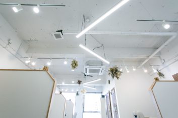 モダンでクリーンなデザインの美容室内装、白い壁と天井に明るい照明とグリーンのアクセントが特徴
