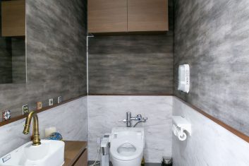 モダンで洗練されたデザインの美容室トイレ内装、木目調キャビネットと大理石調タイル張り