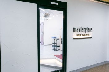 現代風の美容室「masterpiece HAIR WORKS」の入り口、明るく清潔感のある内装でおしゃれなカットステーションが見える