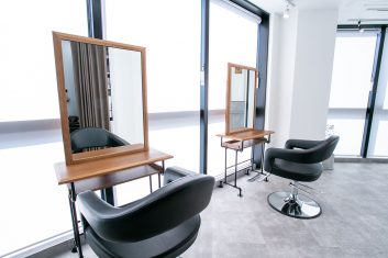 モダンでスタイリッシュな美容室の内装、清潔感のある空間に配置された黒い回転式美容席と、木製フレームの大きな鏡