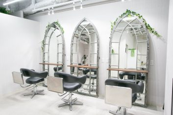 モダンで洗練された美容室の内装、アーチ型の大きな鏡と快適なスタイリングチェア、白い壁と天井に緑の植物がアクセントを加えている空間