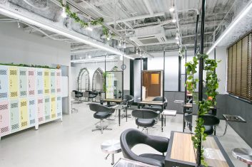 モダンで洗練された美容室の内装、明るく広々とした空間に配置されたスタイリッシュな美容席、天井から垂れ下がる緑の植物がアクセントになったサロン