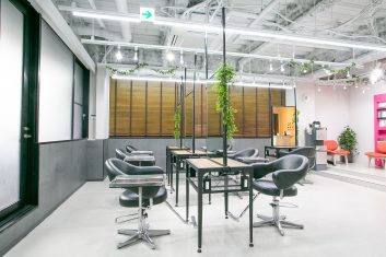 現代的な美容室の内装で、スタイリッシュな黒の椅子とミラーが設置されたカットスペース、天井から吊るされた緑の植物がアクセントになっている明るい雰囲気のサロン
